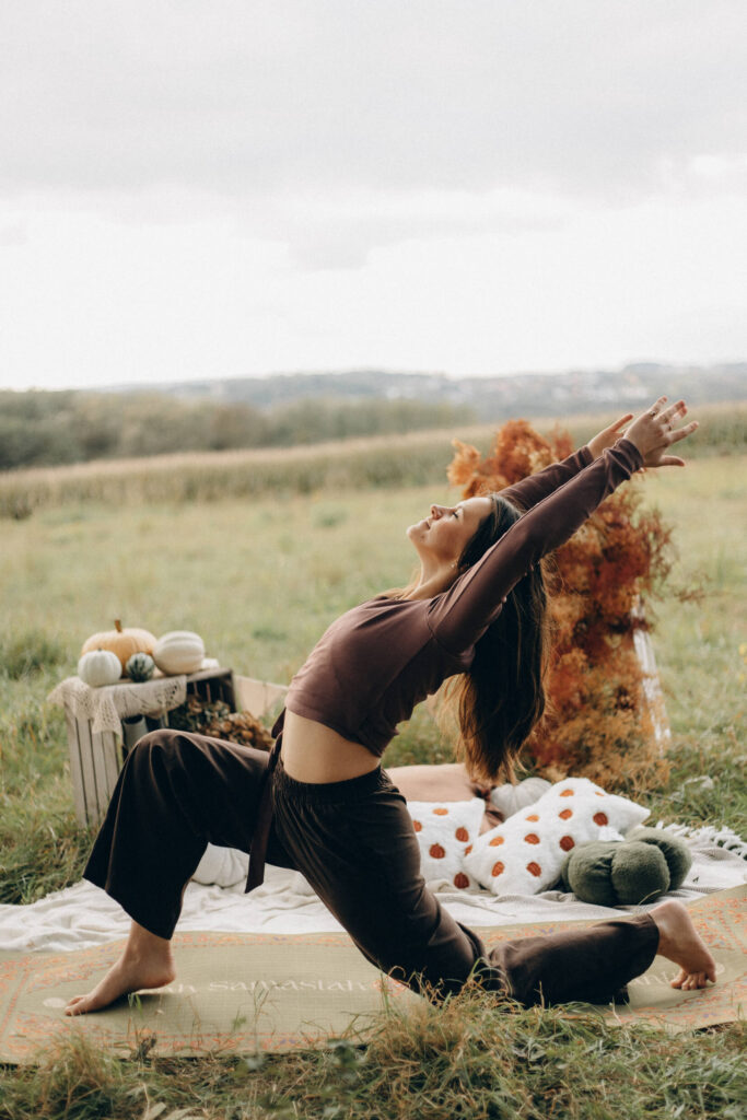 Kamila Natkaniec w pozycji niskiego wykroku (anjaneyasana) z uniesionymi ramionami — joga w plenerze